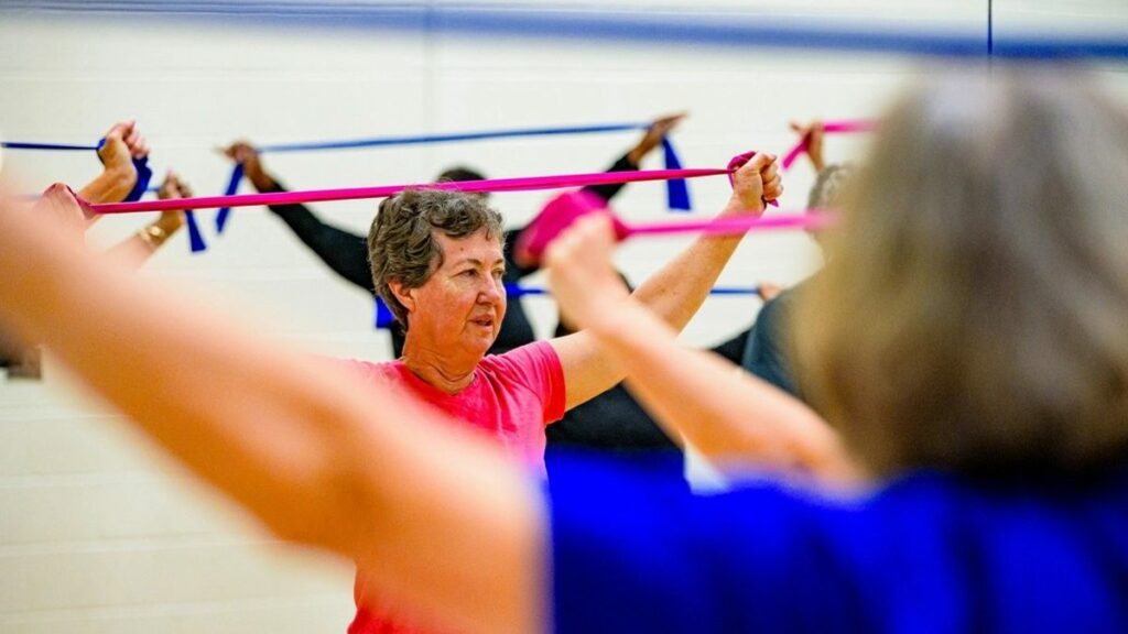 Femme senior faisant un exercice de renforcement des bras avec un élastique lors d'un cours collectif